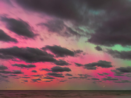 Bunter Dämmerungshimmel über dem Meer mit leuchtend rosa, grünen, auroraähnlichen Lichtern und dunklen Wolken