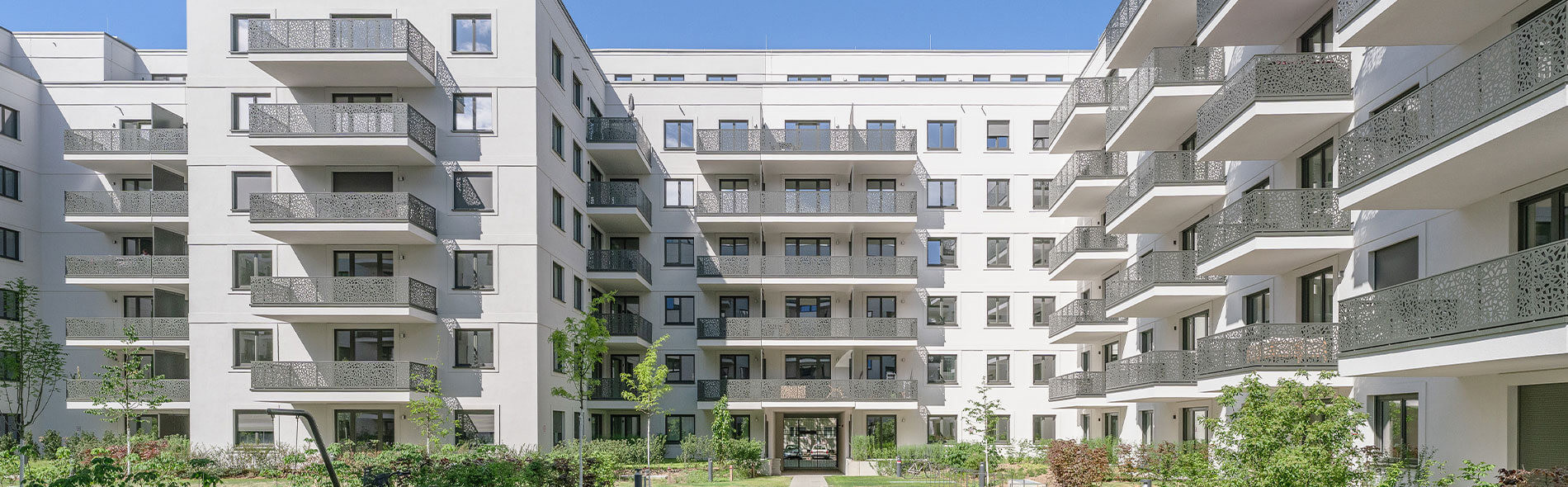 Weißer Wohnkomplex mit Balkonen im Projekt „Am Winterfeldt“ in Berlin-Schöneberg vor blauem Himmel.