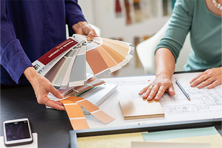 2 Frauen sitzend am Tisch, eine mit Farbfächer in der Hand technische Zeichnung auf dem Tisch