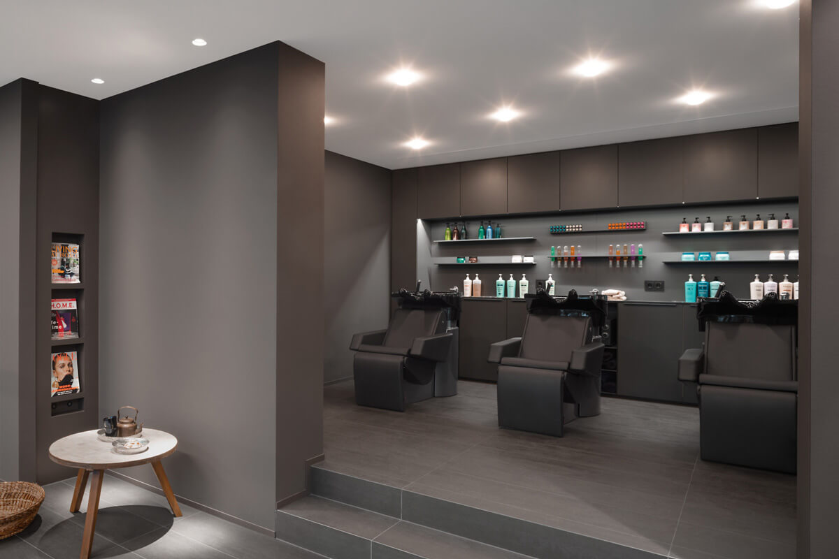 Friseursalon mit grauen Wänden. Im Hintergrund Stühle und Waschbecken