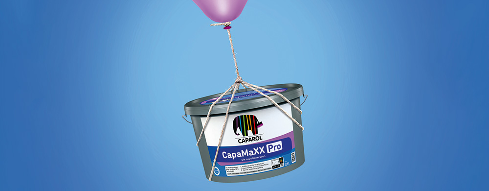 CapaMaXX Farbe schwebt an braunen Seilen mit rosa Ballon vor blauem Hintergrund – Fokus auf Leichtigkeit und Umweltfreundlichkeit.