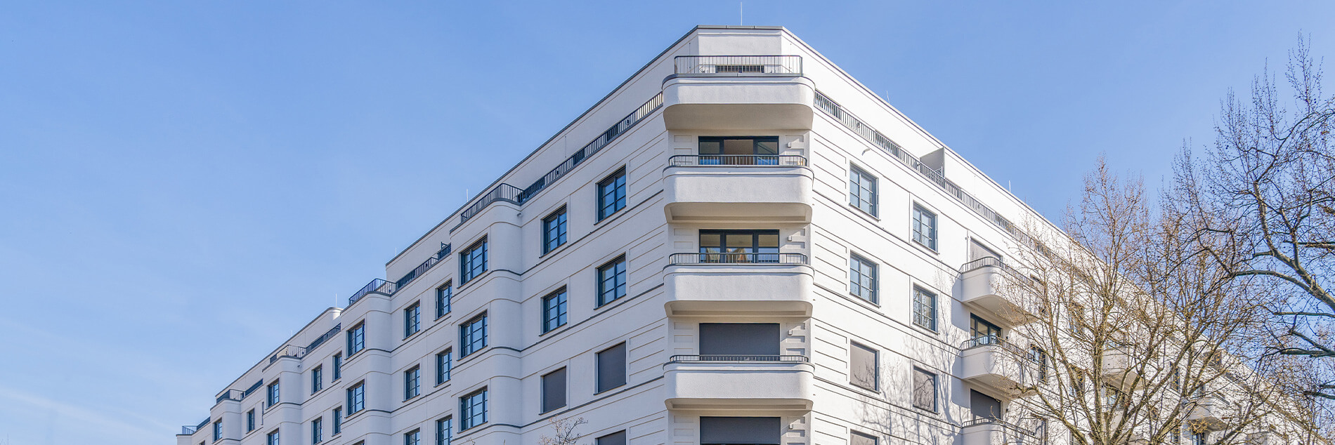 Weißer Wohnkomplex mit Balkonen im Projekt „Am Winterfeldt“ in Berlin-Schöneberg vor blauem Himmel.