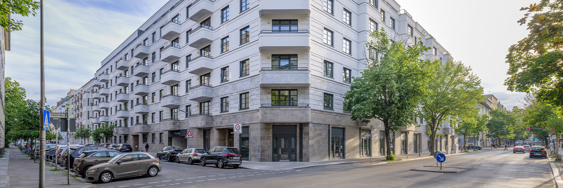 Weißes Miethaus mit Balkonen im Projekt „Am Winterfeldt“ in Berlin-Schöneberg, umgeben von Bäumen und parkenden Autos an der Straße.
