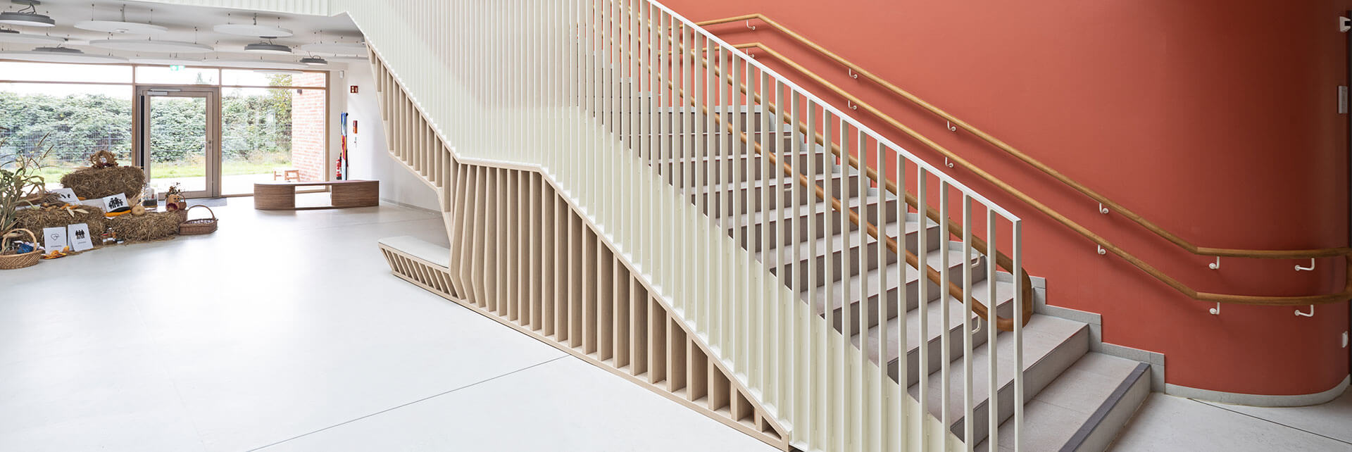 Treppenaufgang im Neubau der Kindertagesstätte in Ralbitz-Rosenthal vor farbiger Wand und Fensterfront im Hintergrund.