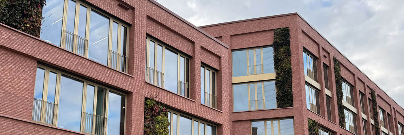 Fassade aus rötlichen Klinkerriemchen mit Fensterfront des Quartiers Q8 Neckarpark in Stuttgart mit blauem Himmel.