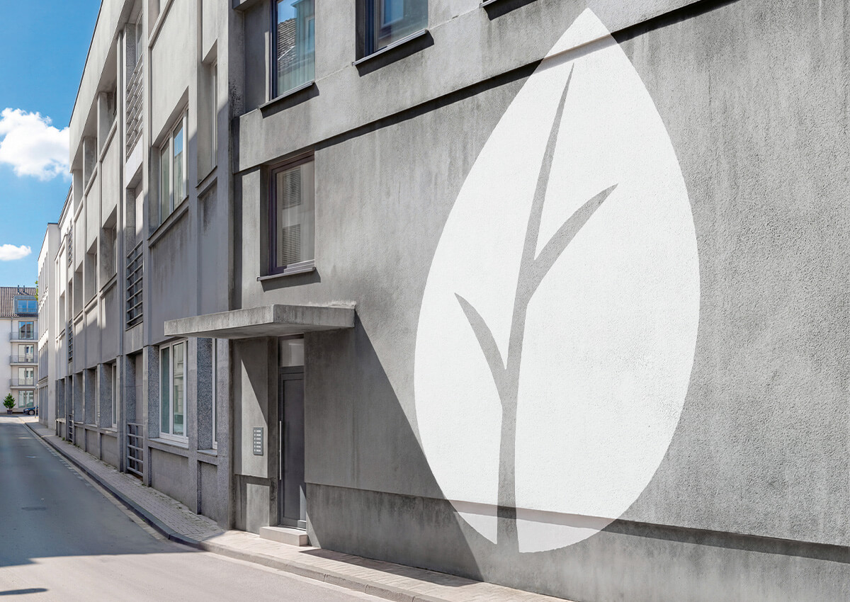 Großes weißes Blatt mit stilisiertem Ast als Wandgrafik auf grauer Hauswand neben einem Hauseingang in einer ruhigen Straße