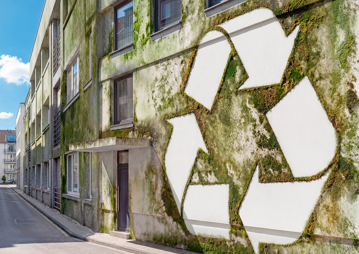 Großes Recycling-Symbol aus Moos an einer Hauswand in einer engen Stadtstraße